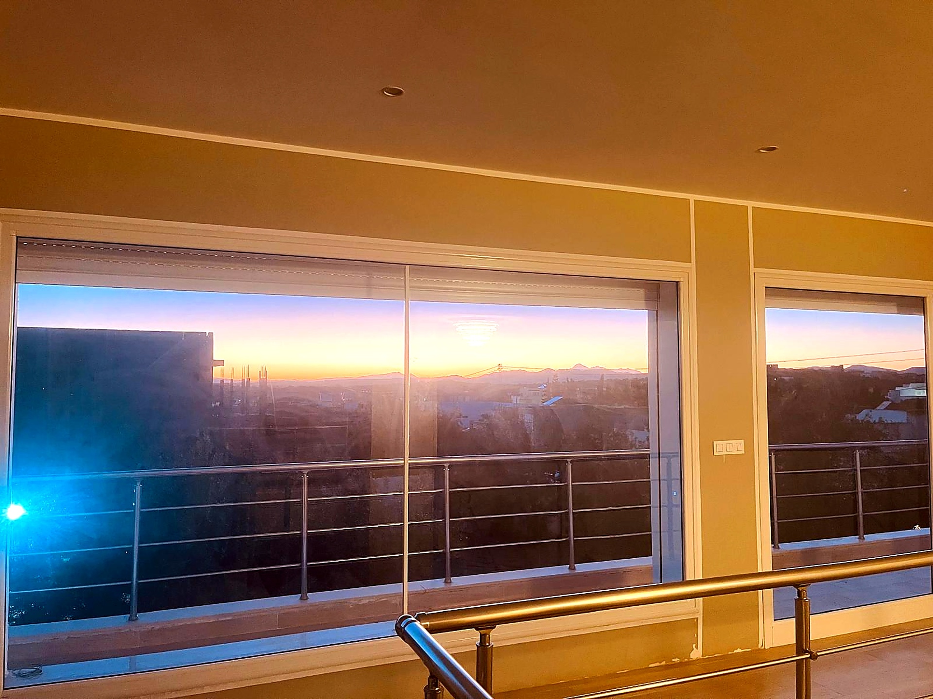 Panoramic sliding windows framing a golden sunset over the hills