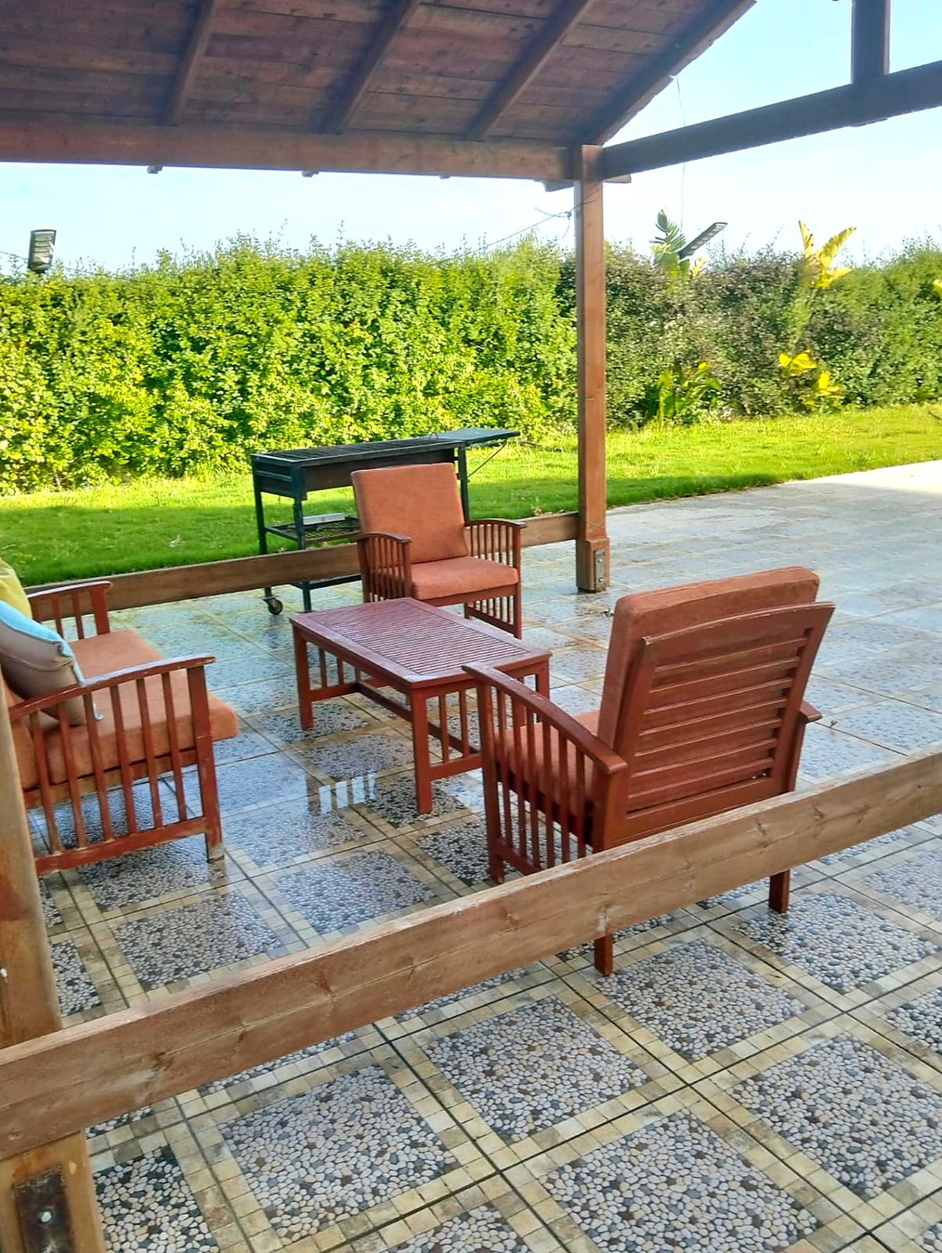 Shaded pergola lounge with teak seating and barbecue beside the lawn