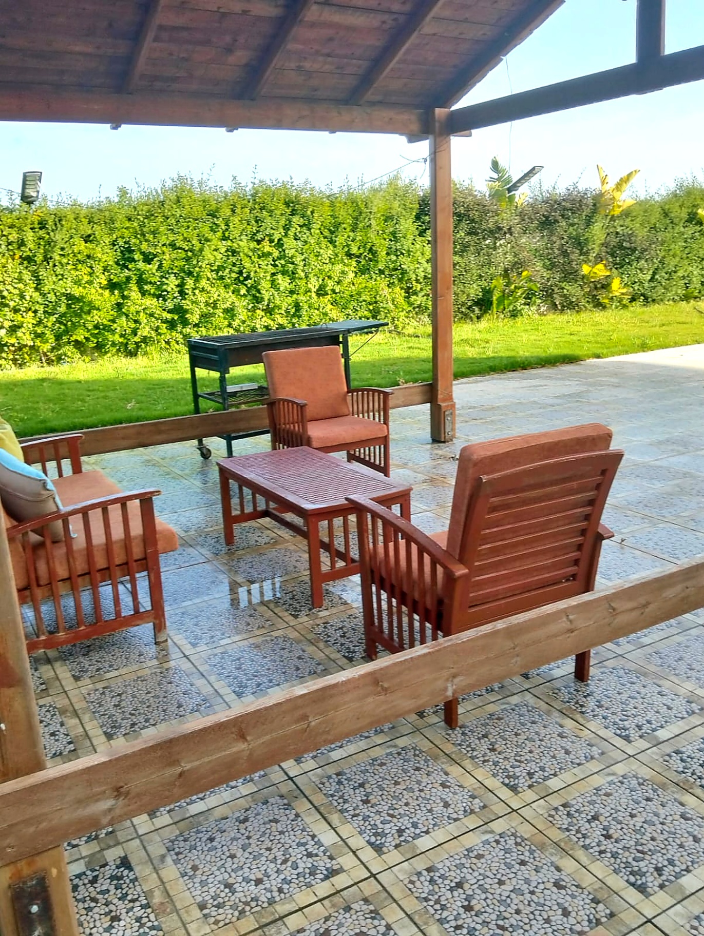 Shaded pergola lounge with teak seating and barbecue beside the lawn